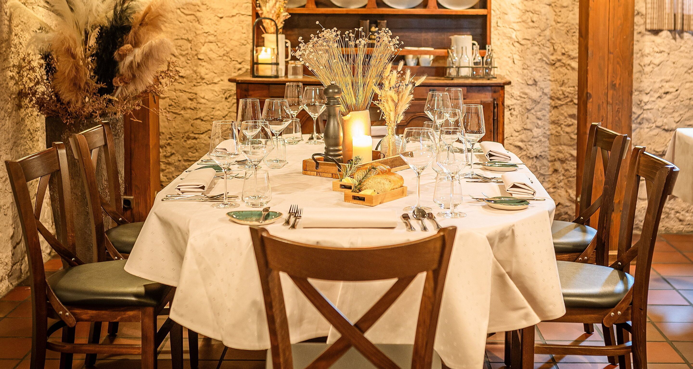 A dining table set with multiple wine glasses, plates, and cutlery, surrounded by wooden chairs.