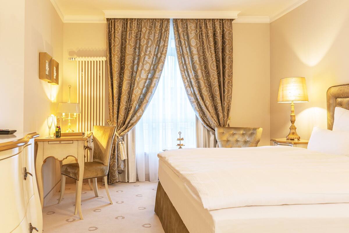Une chambre d’hôtel avec un lit, un bureau, une chaise, une télévision et des rideaux.