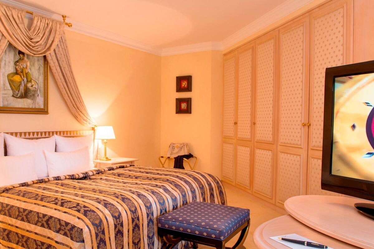 Une chambre d’hôtel comprenant un lit, une télévision, un bureau avec une lampe, une chaise et une armoire.