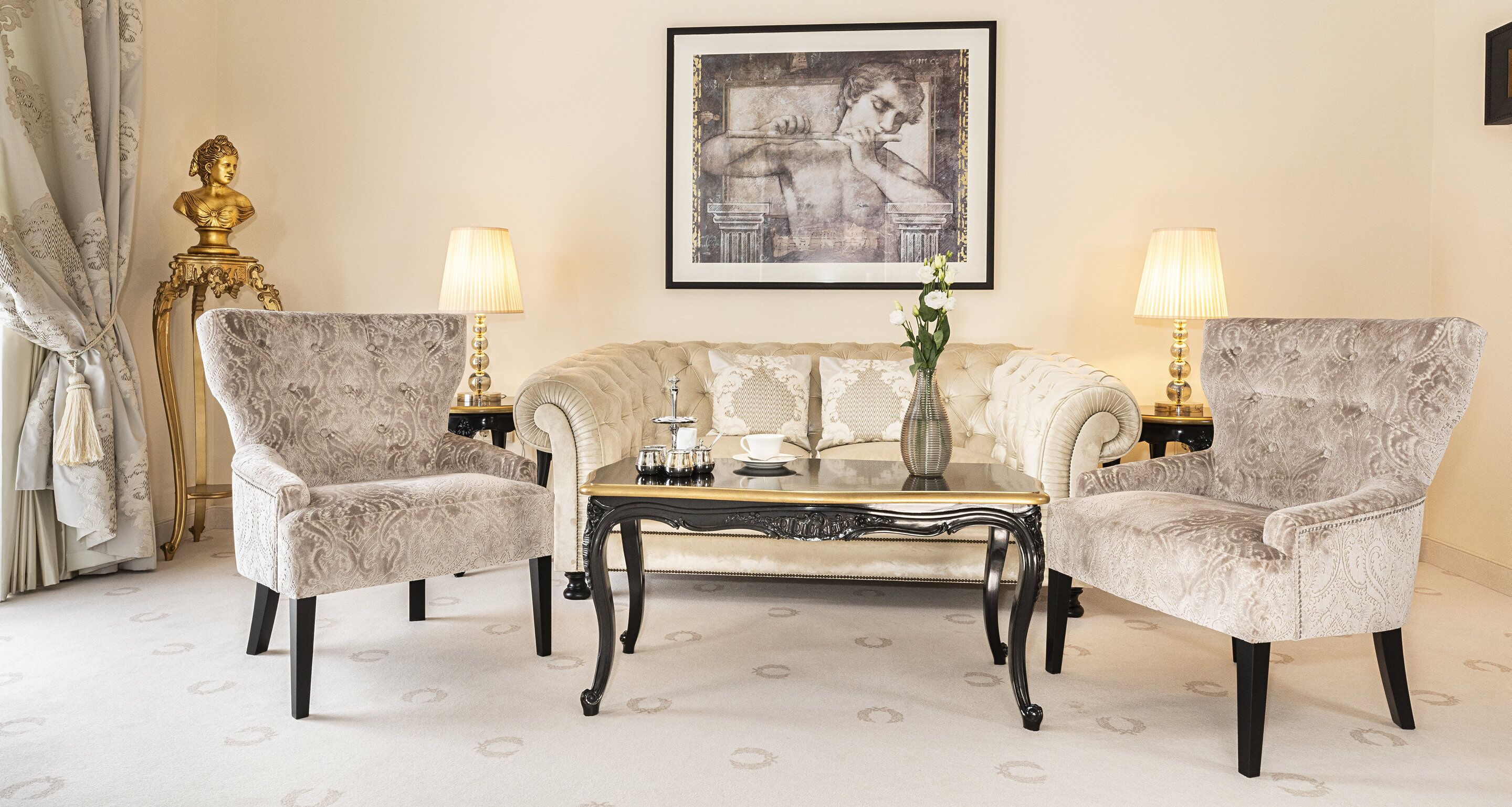 A room with a tufted sofa, two armchairs, a glass coffee table, and two lamps.