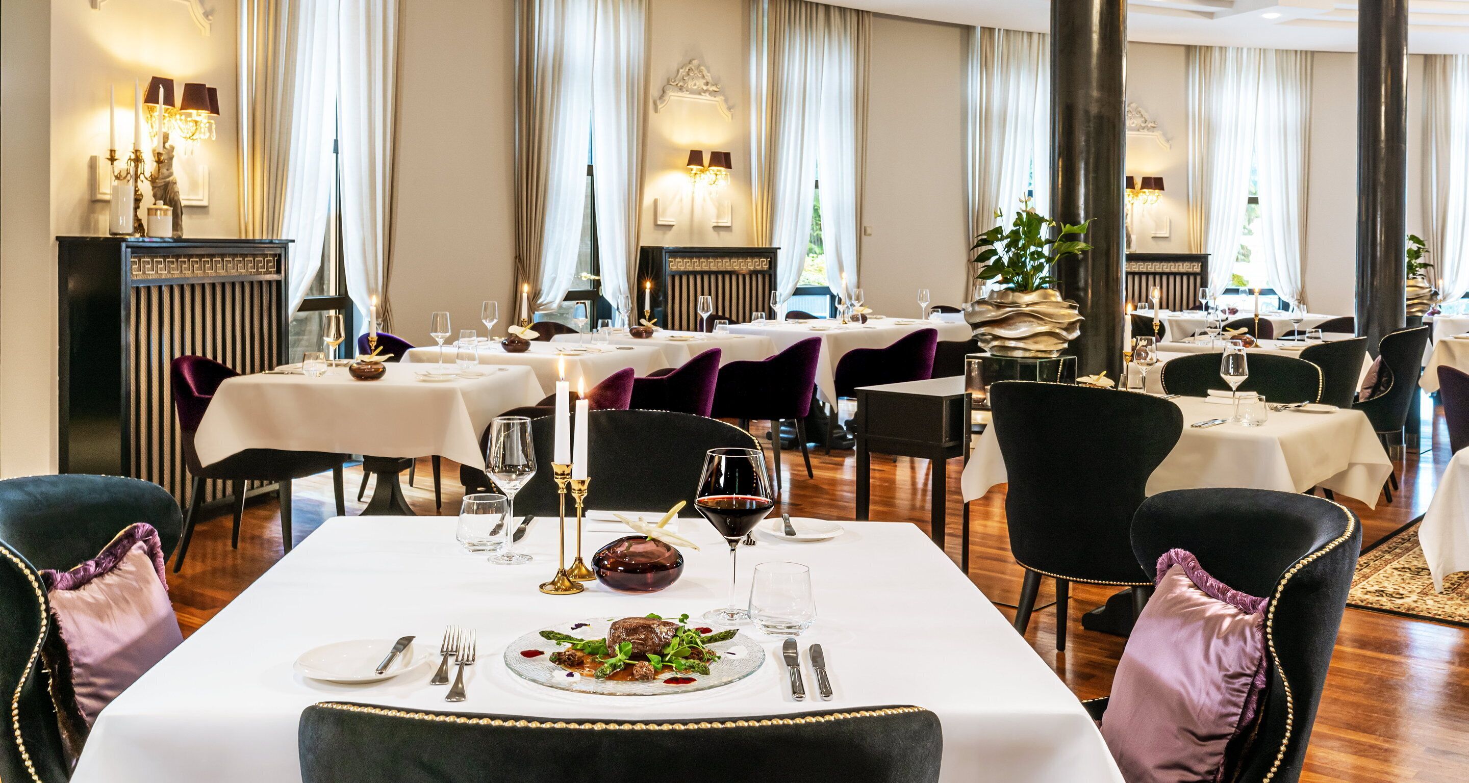 Un restaurante con varias mesas, cada una con mantel blanco, sillas negras y velas.