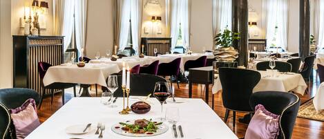 Un restaurante con varias mesas, cada una con mantel blanco, sillas negras y velas.
