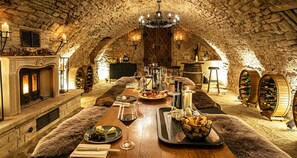 Un comedor acogedor con paredes de piedra, una larga mesa de madera dispuesta para una comida, velas y botellas de vino.