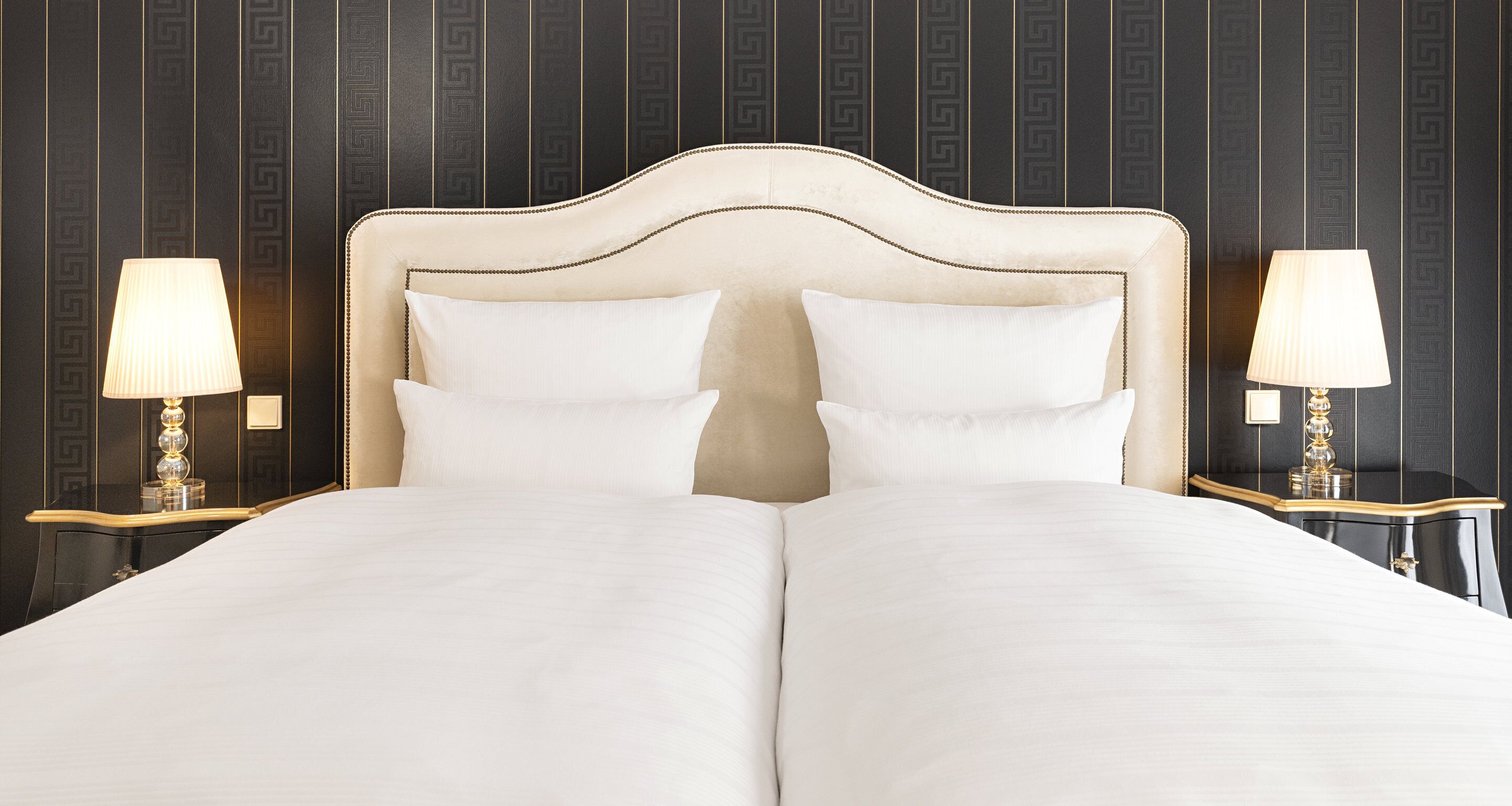 A double bed with a white headboard and two white pillows, flanked by two bedside tables with lamps.