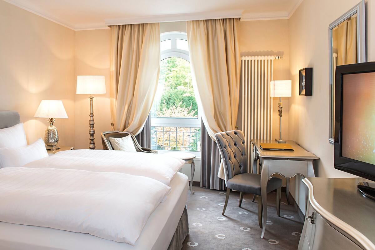 Une chambre d’hôtel avec deux lits, un bureau, une chaise, une télévision et une fenêtre avec des rideaux.