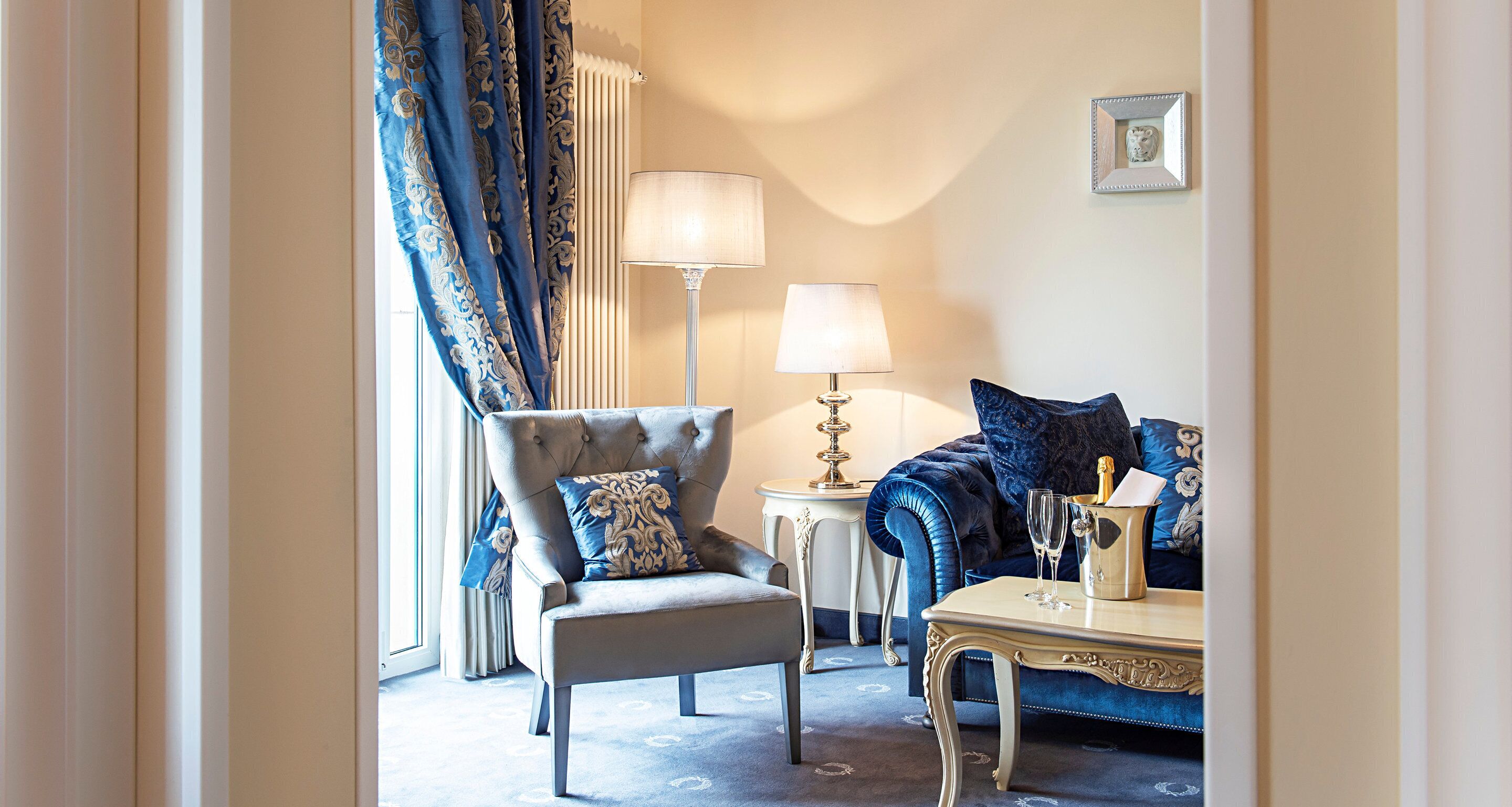 A room with a grey upholstered armchair, a blue sofa, a small table with a lamp, and a picture on the wall.