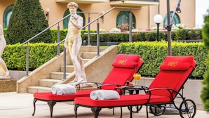 Zona de piscina con sillas reclinables rojas, una estatua y una escalera.