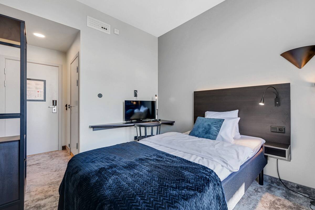 A modern hotel room with a bed, a desk, and a TV.
