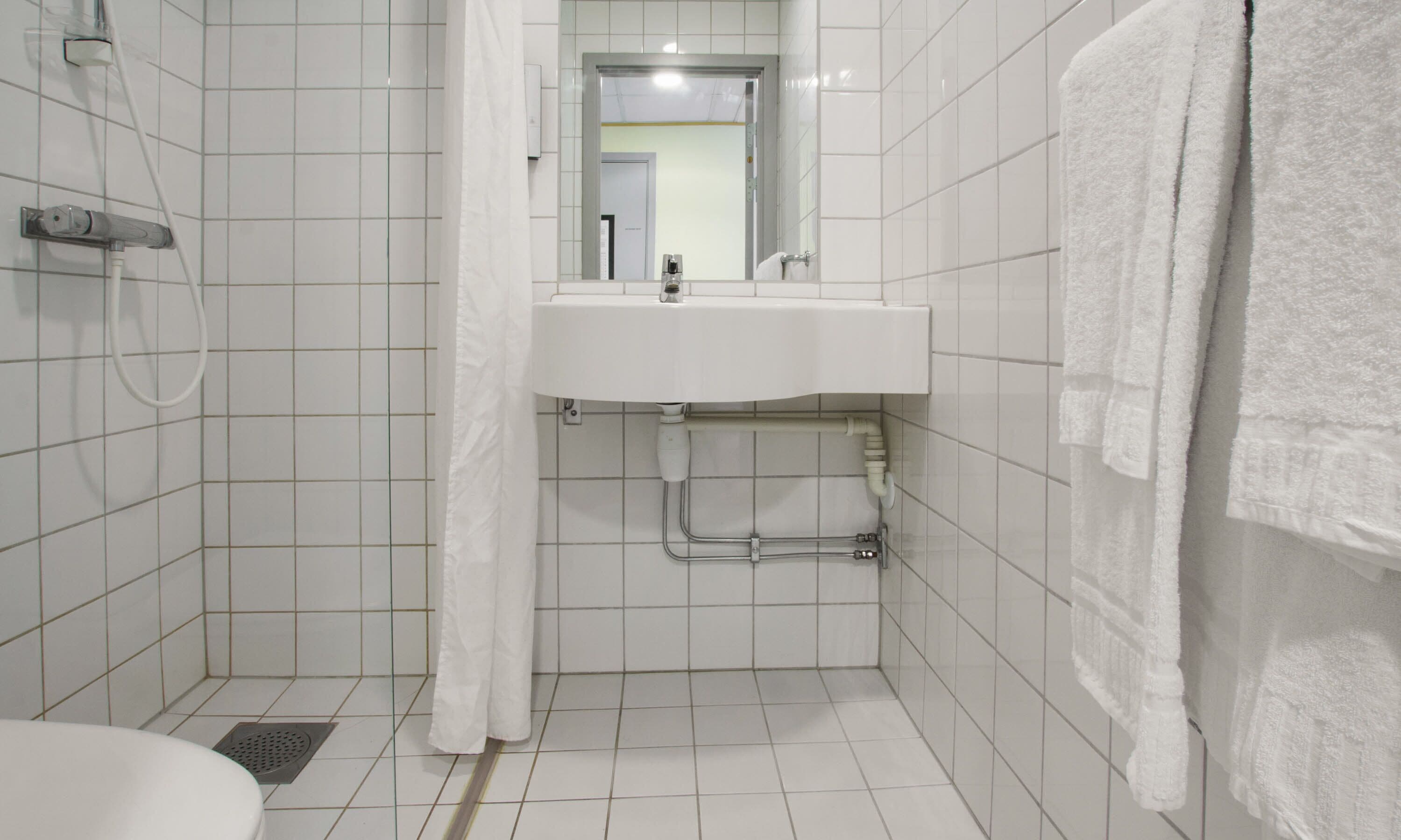 A small, clean bathroom with a white sink, a shower, and a toilet.