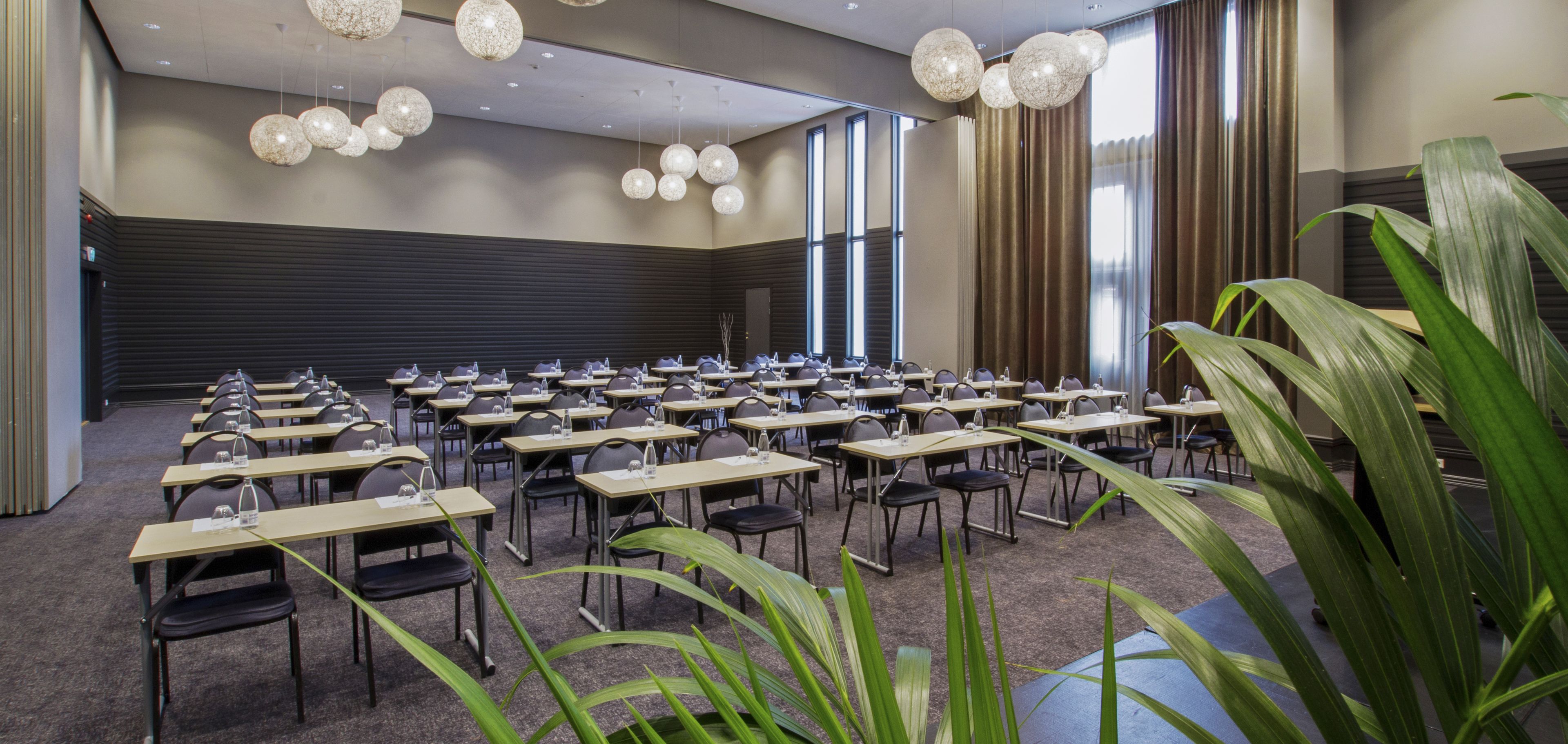 A conference room with multiple tables and chairs, large windows, and hanging spherical light fixtures.
