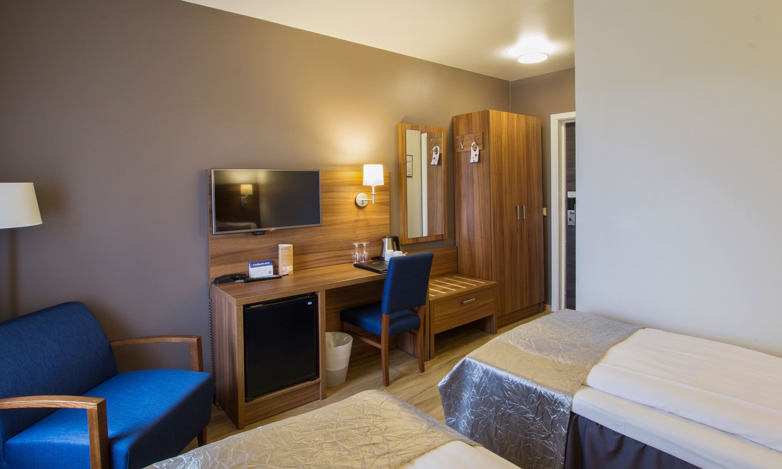 A hotel room with a bed, a desk, a chair, a television, and a wardrobe.
