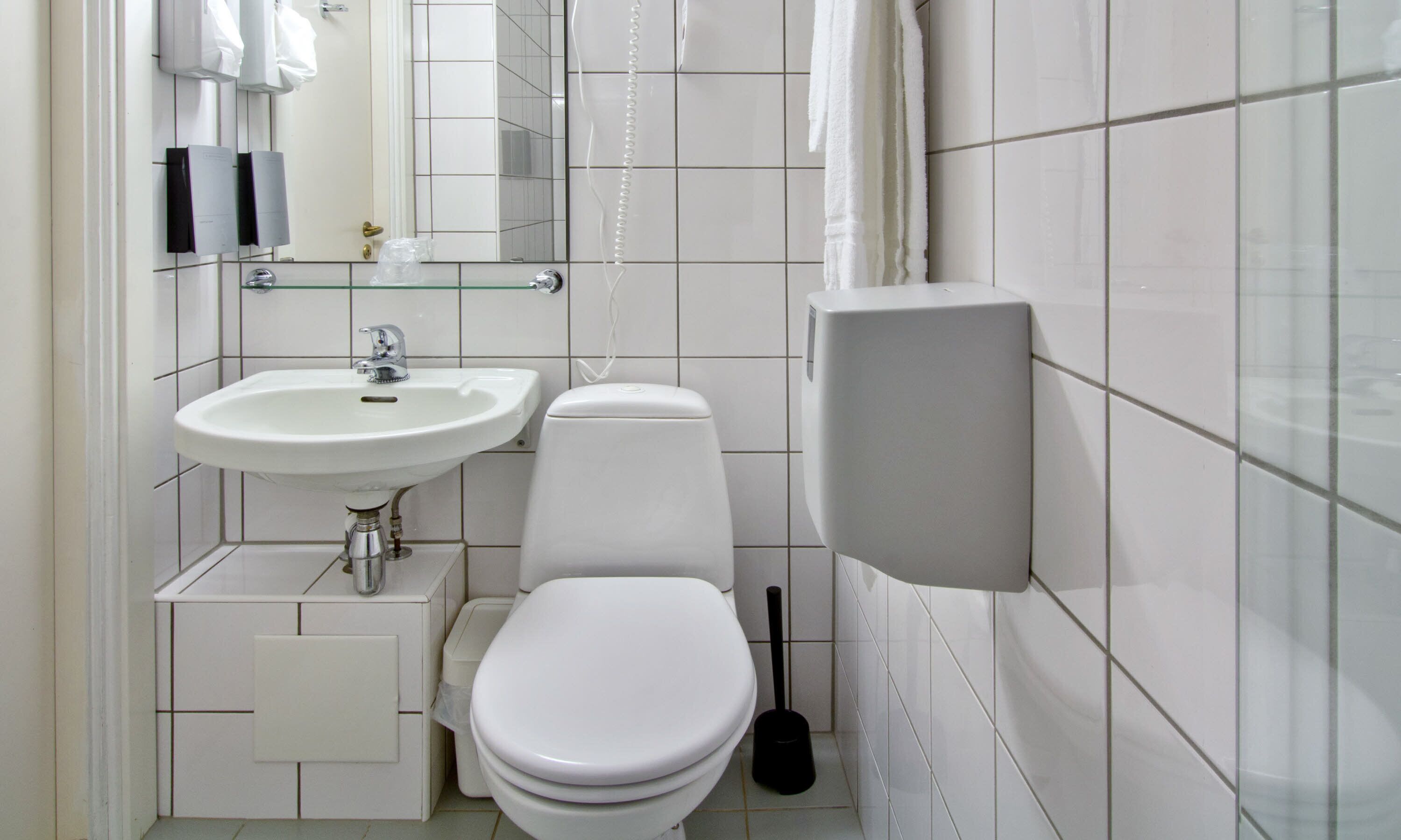 A compact bathroom with a white sink, toilet, and a hand dryer mounted on the wall.