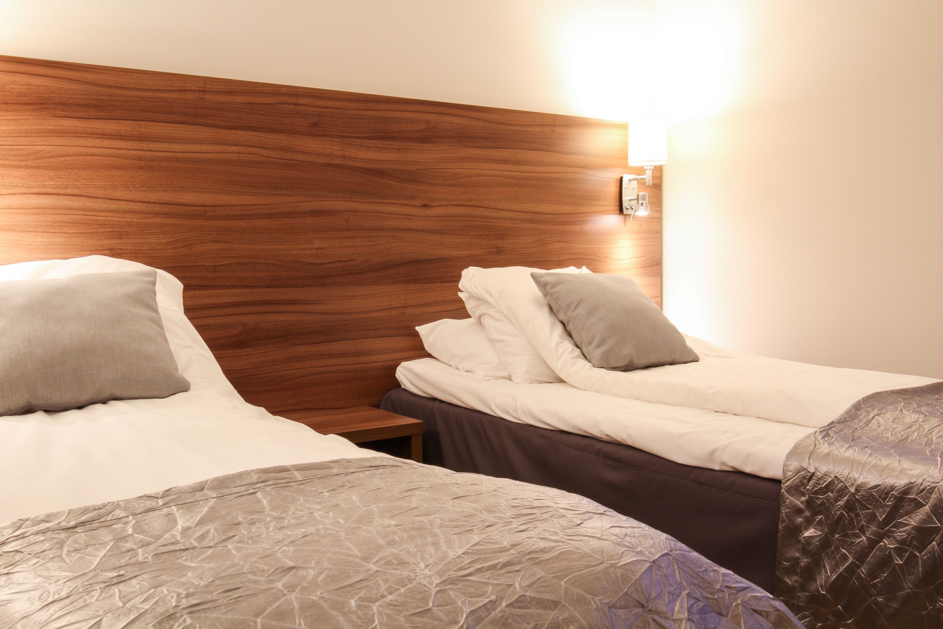 A hotel room with two beds, wooden headboard, and a nightstand with a lamp.