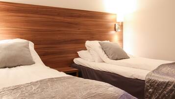 A hotel room with two beds, wooden headboard, and a nightstand with a lamp.