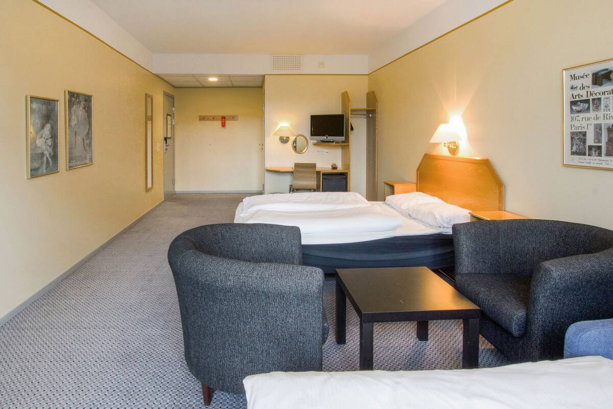 A hotel room with two beds, a desk, a chair, and a TV.