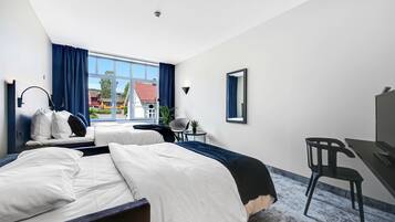 A hotel room with two beds, a desk, a chair, a small table with a plant, and a window with curtains.