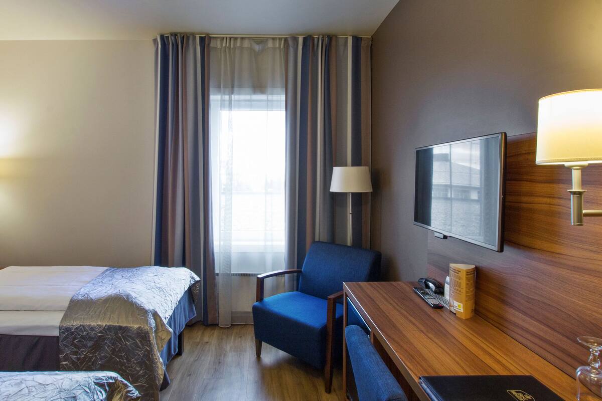 A hotel room with two beds, a desk with a chair, a television, and a window with curtains.