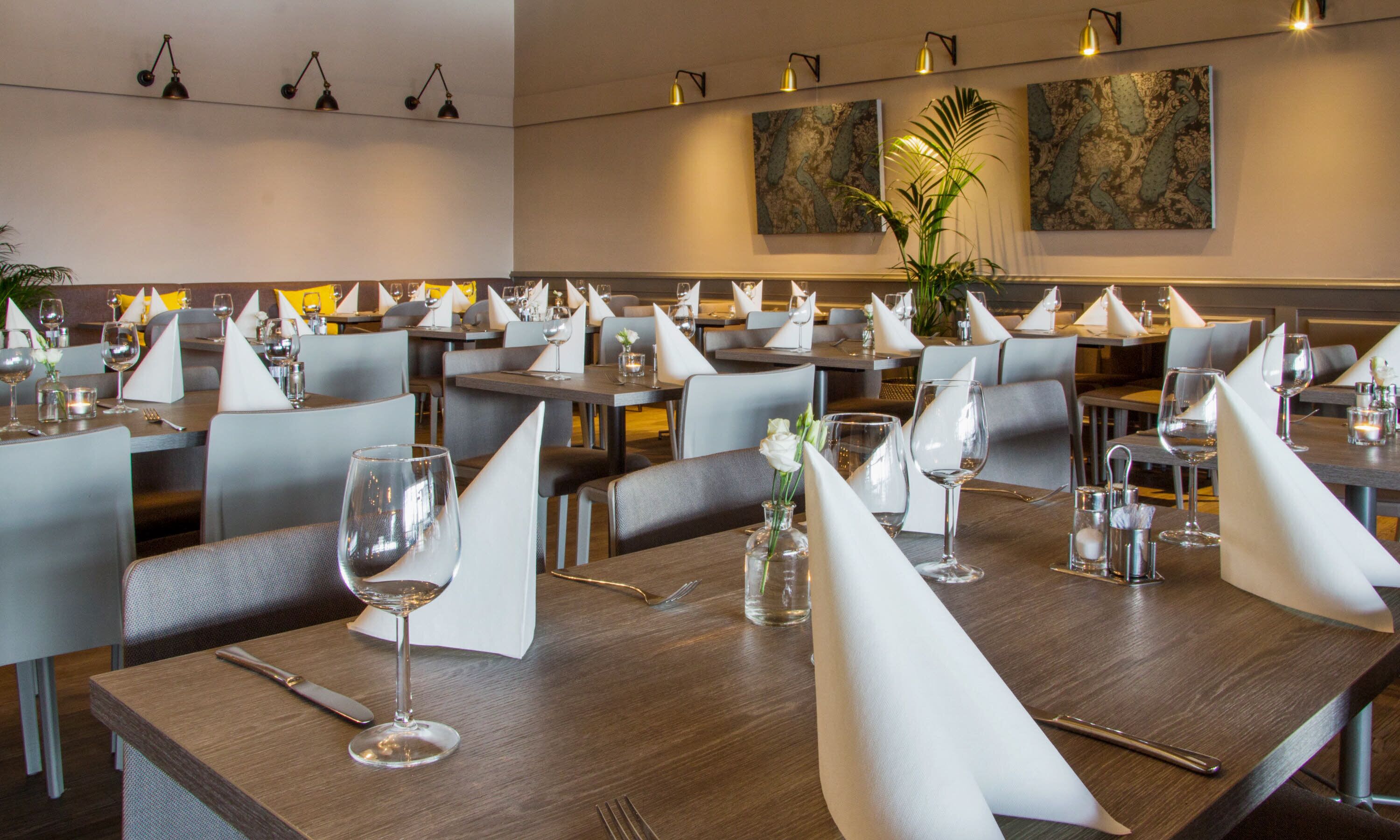 Un restaurante con varias mesas dispuestas para comer, cada una con servilleta blanca, copa de vino y cubiertos.