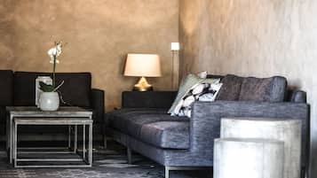Una sala de estar moderna con un sofá gris, una pequeña mesa de centro con un jarrón y una planta, y una lámpara sobre una mesita auxiliar.