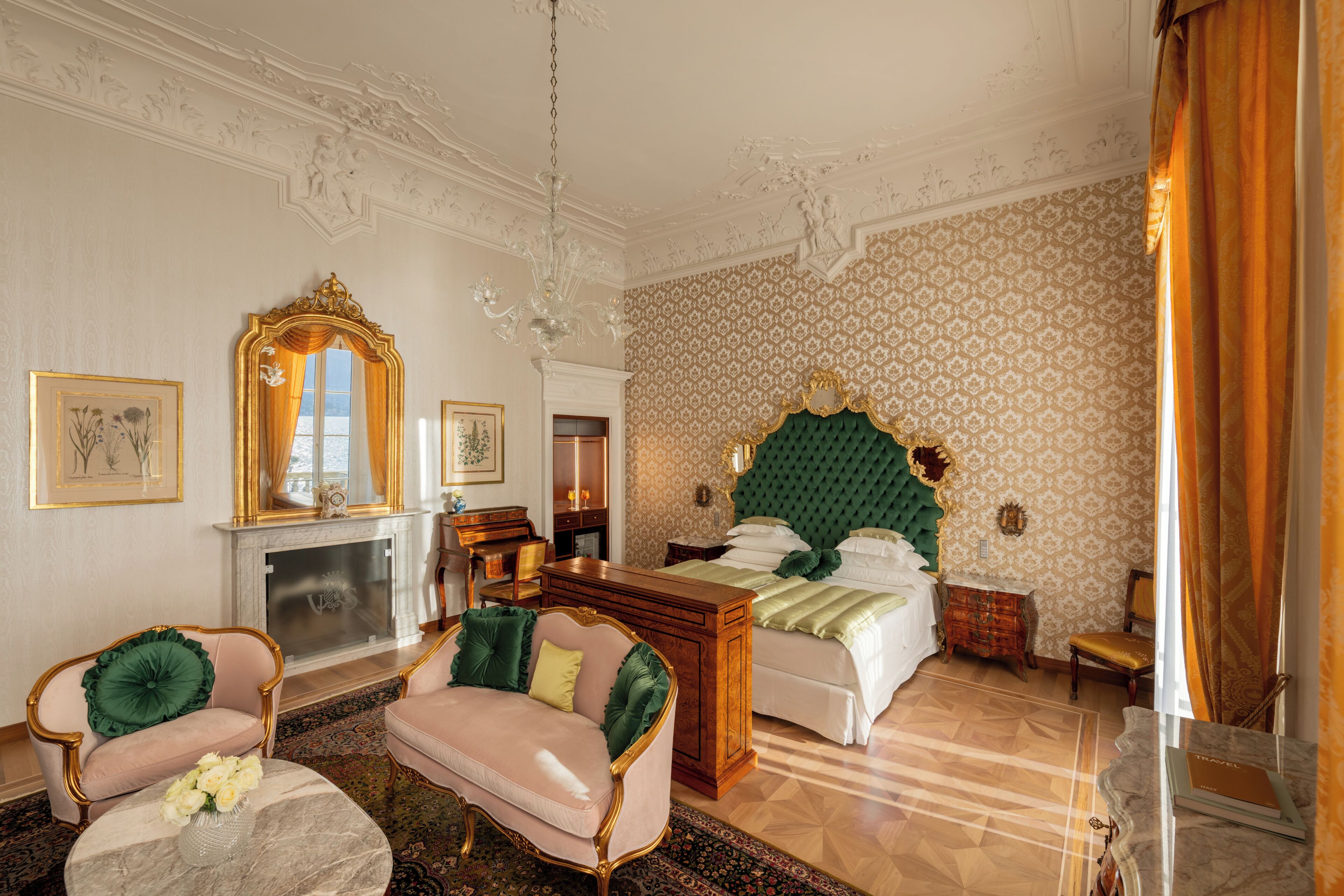 A room with a bed, two armchairs, a fireplace, and a mirror.