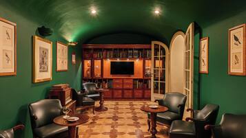 A room with a green wall, a bookshelf, a television, leather chairs, and a patterned floor.