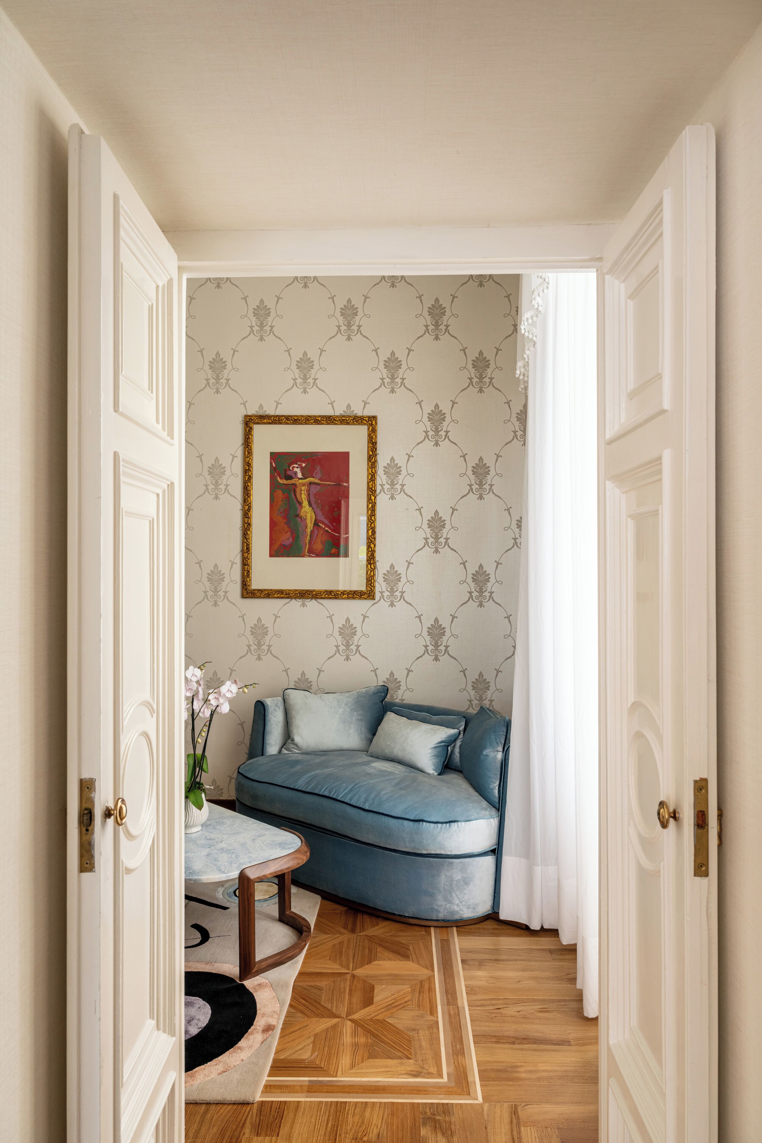 A room with a blue sofa, a patterned wallpaper, and a framed artwork on the wall.