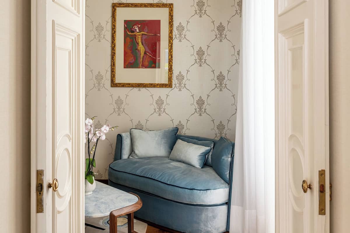 A room with a blue sofa, a patterned wallpaper, and a framed artwork on the wall.