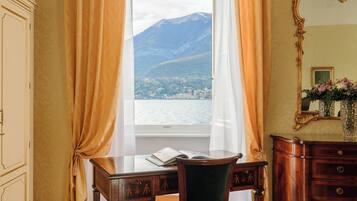 A room with a desk, chair, and a view of a lake and mountains through a window.