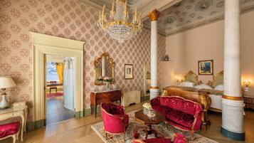Una habitación lujosa con una imponente araña, muebles ornamentados y una cama grande con detalles dorados.