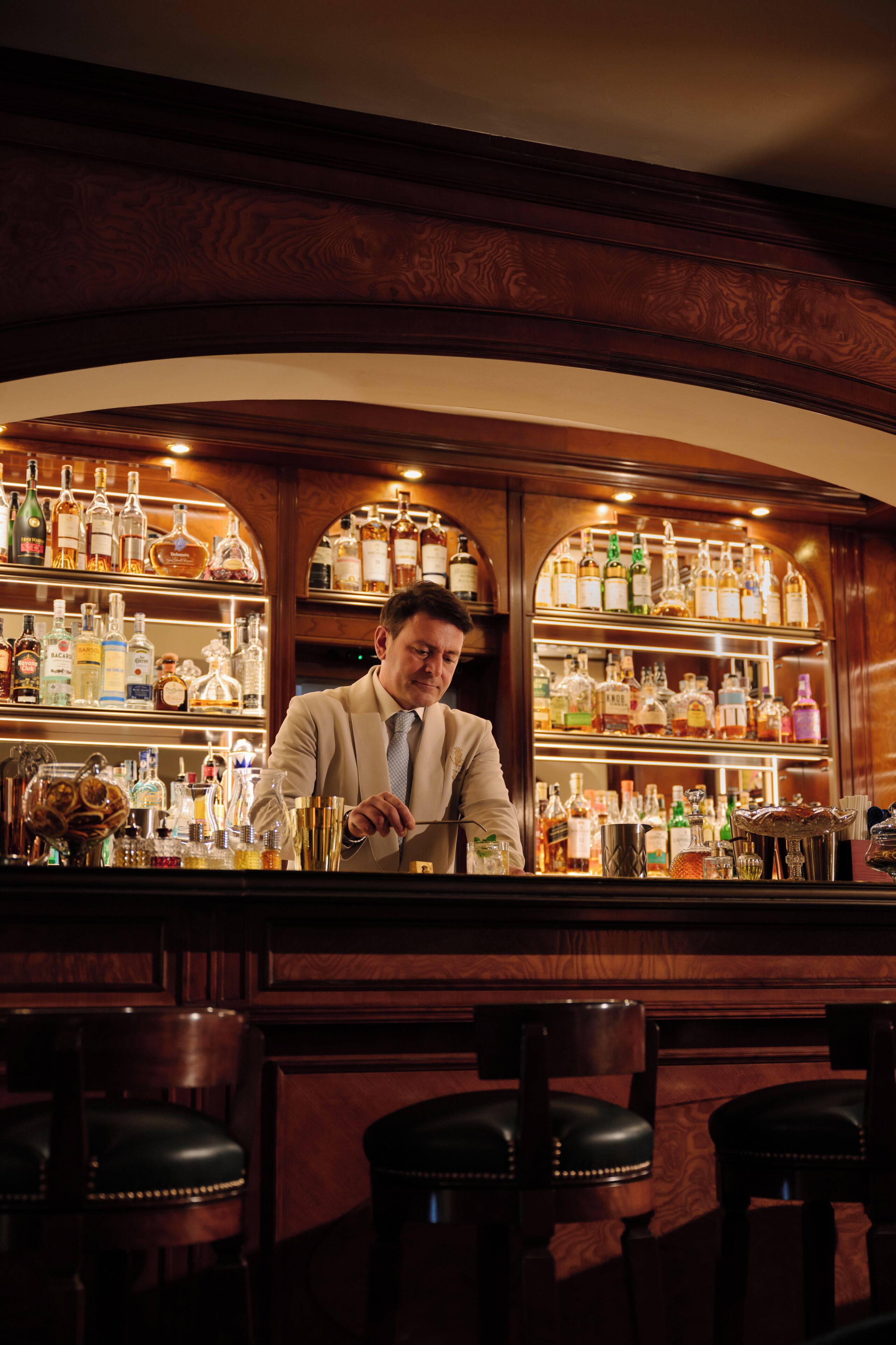 A bar with a bartender, wooden bar counter, and shelves of liquor bottles.