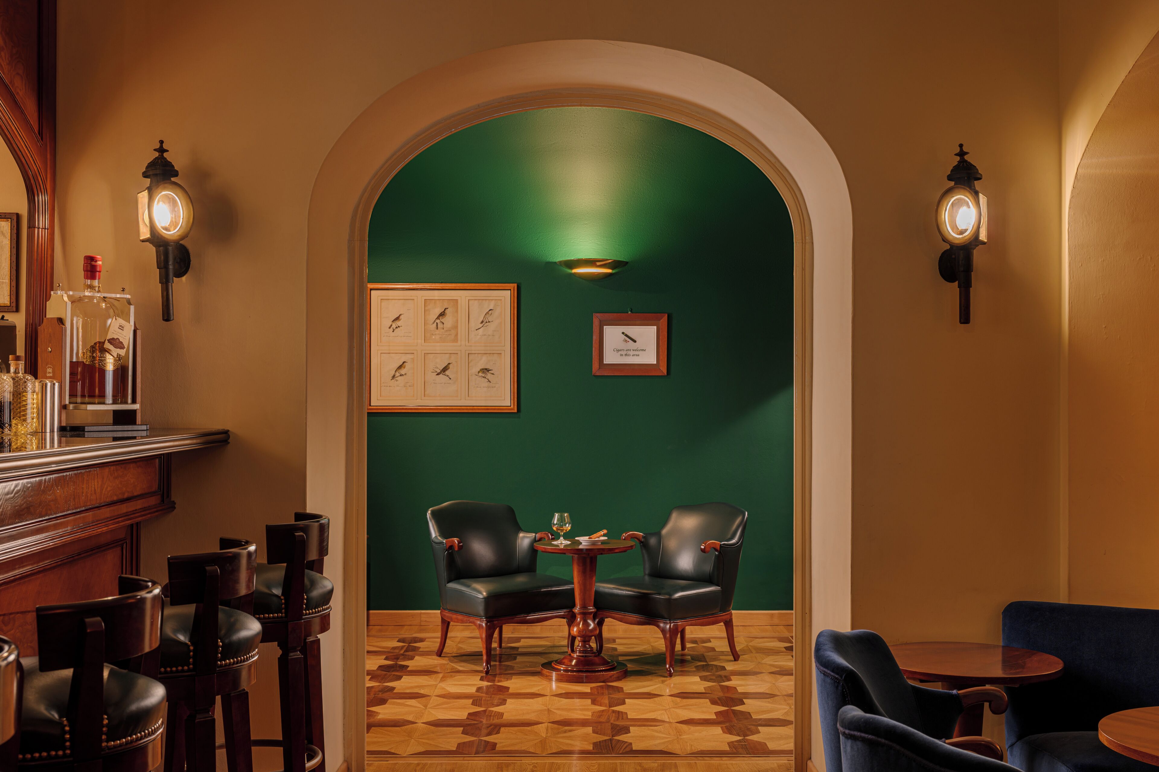 A bar area with wooden bar stools, a round wooden table, and two leather chairs.