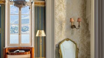 Una habitación con vista al exterior por una ventana, un espejo, una lámpara y un banco.
