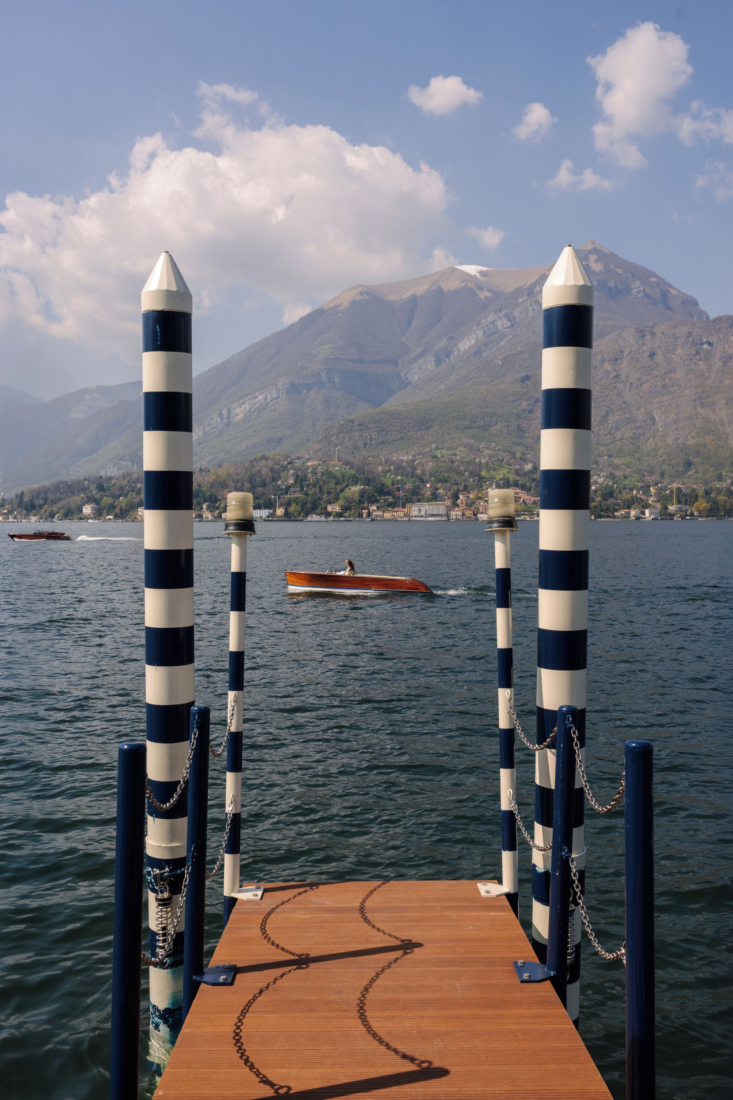 A wooden dock with striped poles, a boat, and a mountain in the background.