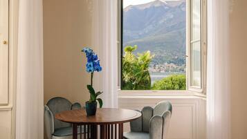 A room with a round table, two chairs, a vase with a blue flower, and a window with a mountain view.
