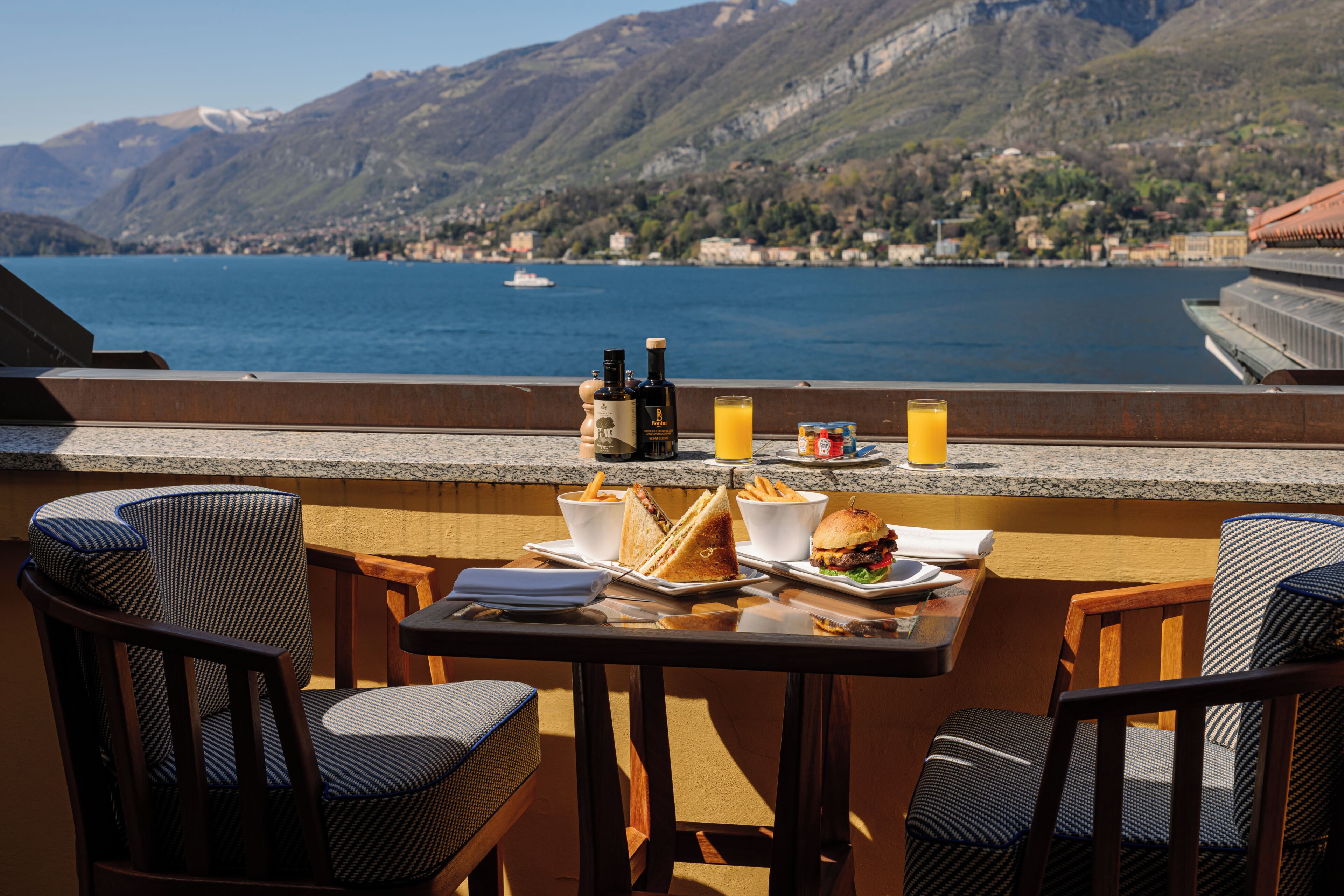 A terrace with a table set for two, overlooking a lake with mountains in the background.