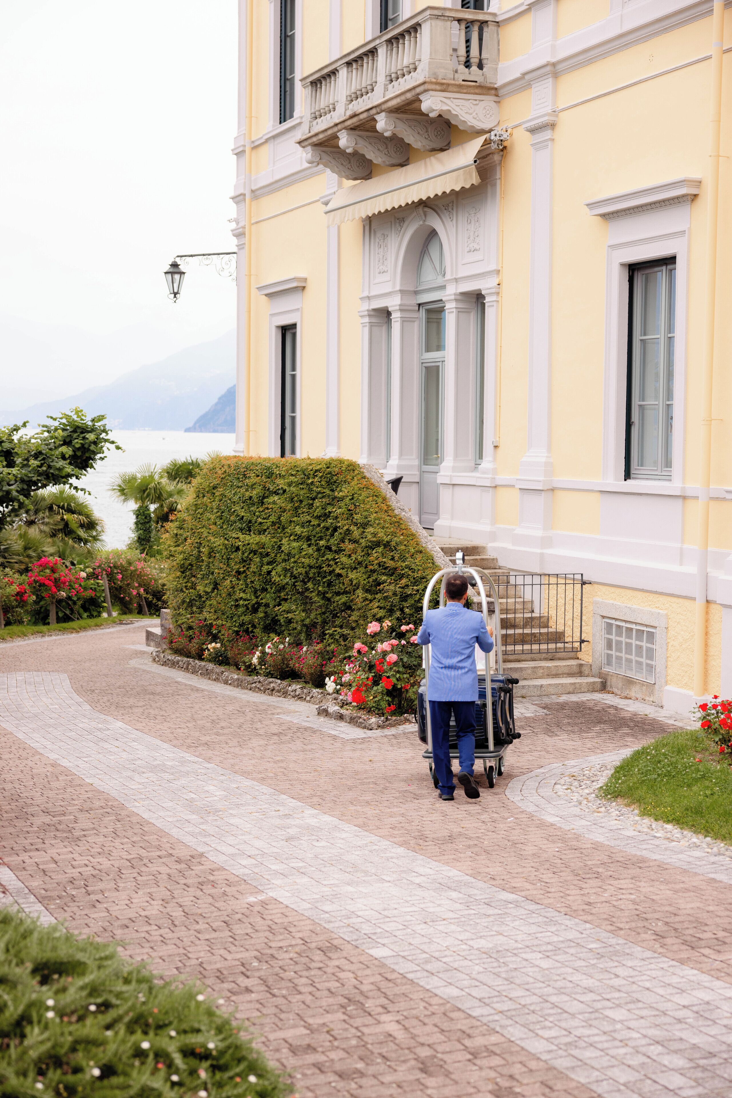 Une personne pousse un chariot à bagages en direction d’un bâtiment doté d’un balcon et offrant une vue sur la mer.