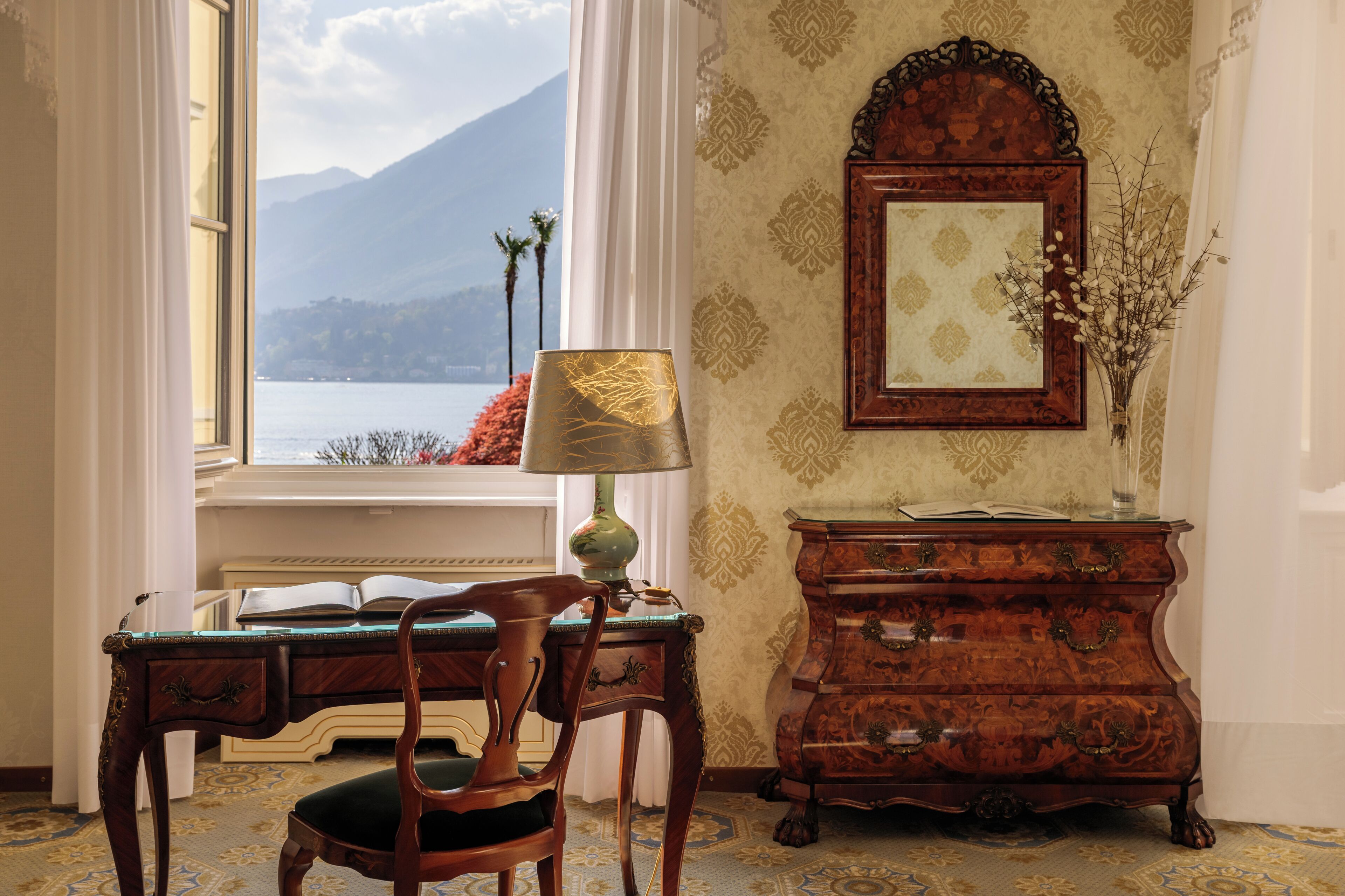 Een kamer met een bureau, stoel, lamp, dressoir en een grote spiegel.