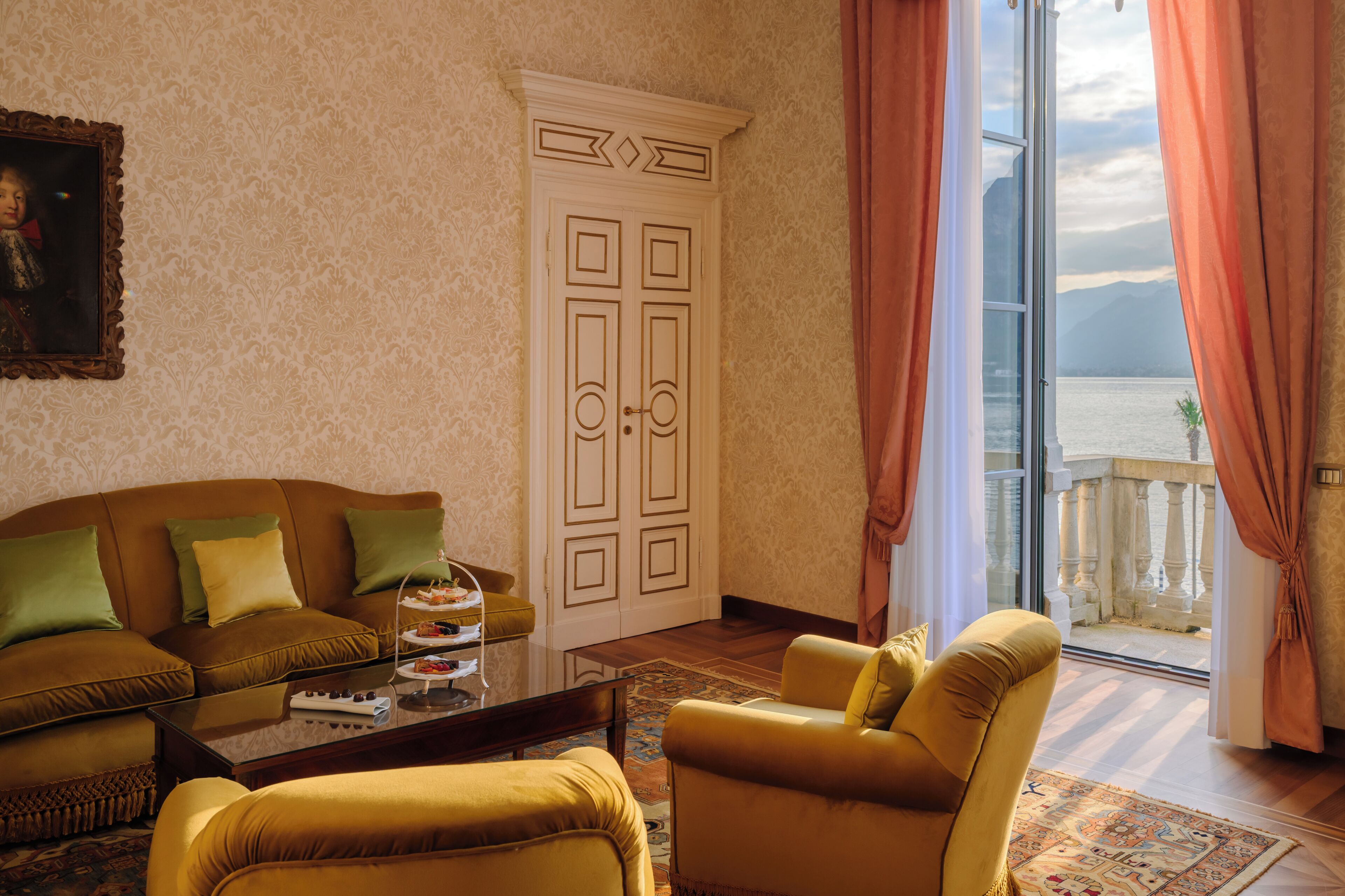 A living room with a sofa, armchairs, a coffee table, a cabinet, and a view of a body of water through a glass door.
