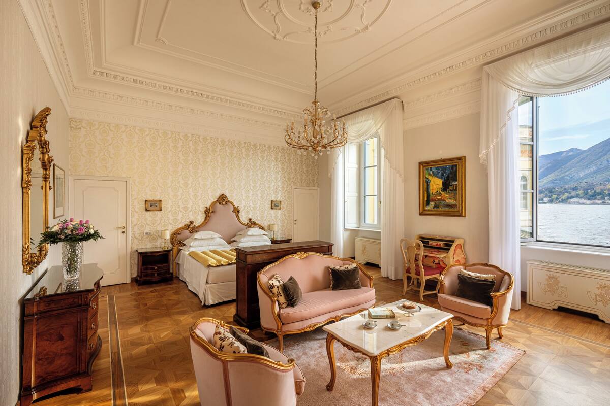 Une pièce comprenant un lit, un canapé, une chaise, une table, un miroir et une fenêtre donnant sur un paysage agréable.