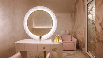 A bathroom with a round mirror, vanity, and a pink chair.