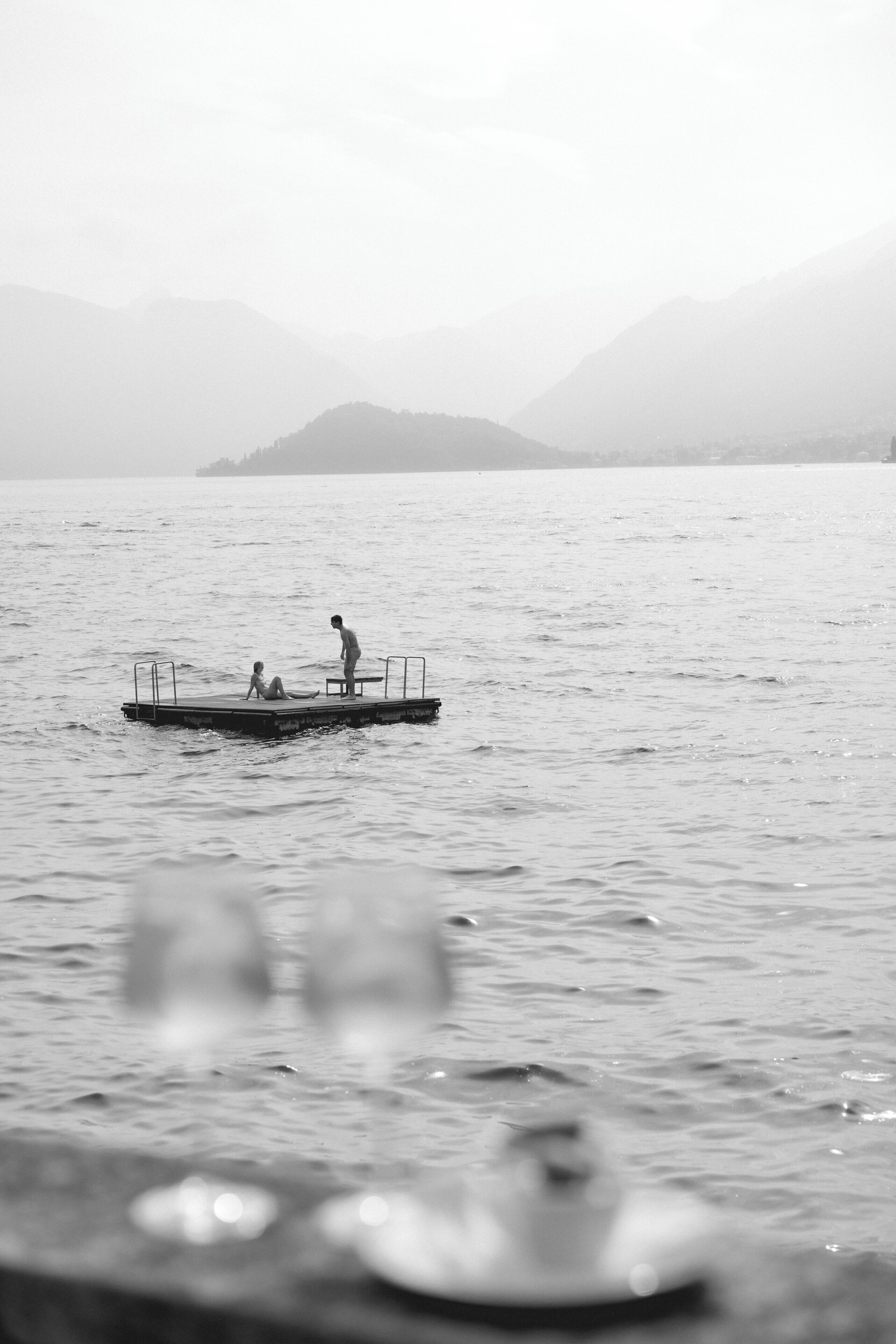 Ein ruhiger See mit einer Anlegestelle und zwei Personen darauf.