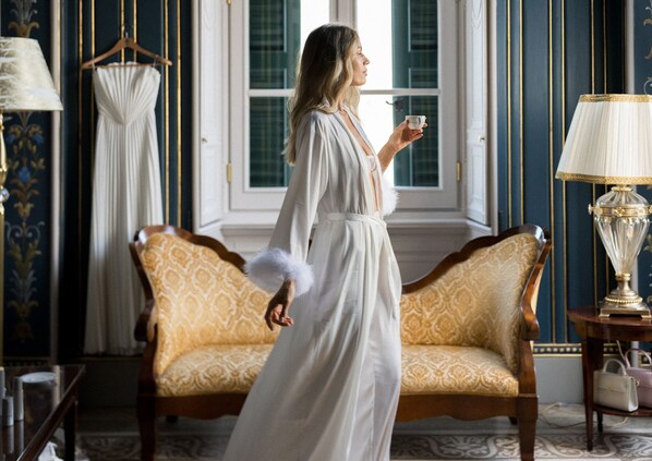 A room with a large window, a sofa, a lamp, and a hanging garment.