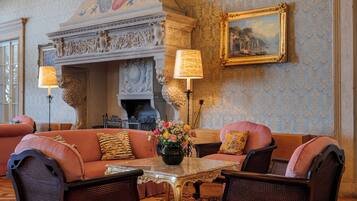 A room with a fireplace, a sofa set, a table with a vase of flowers, and a framed painting on the wall.