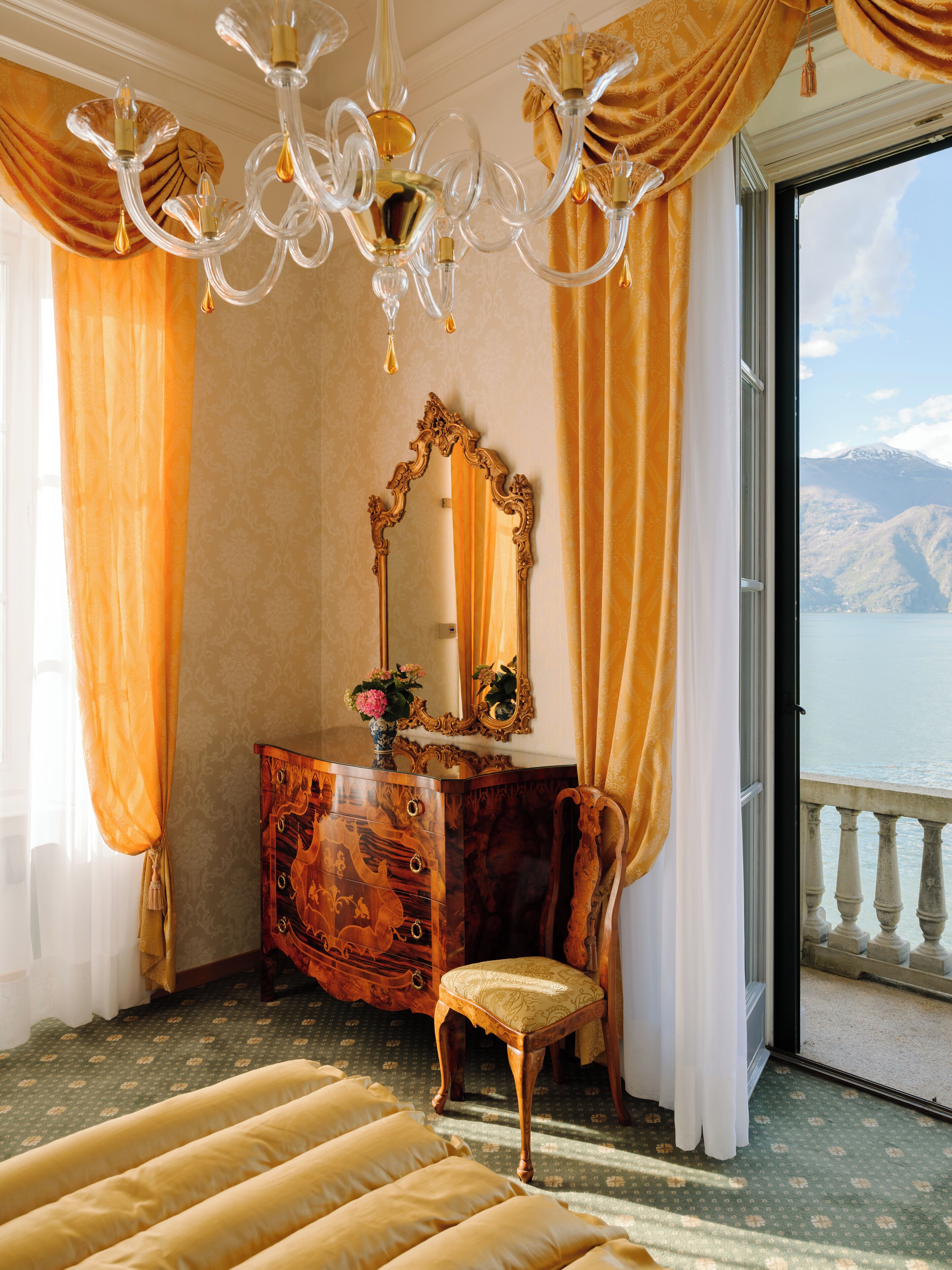 Un dormitorio lujoso con una cama grande, un aparador de madera, un espejo y vistas a un lago y montañas.