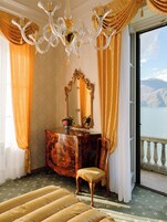 A luxurious bedroom with a large bed, a wooden dresser, a mirror, and a view of a lake and mountains.