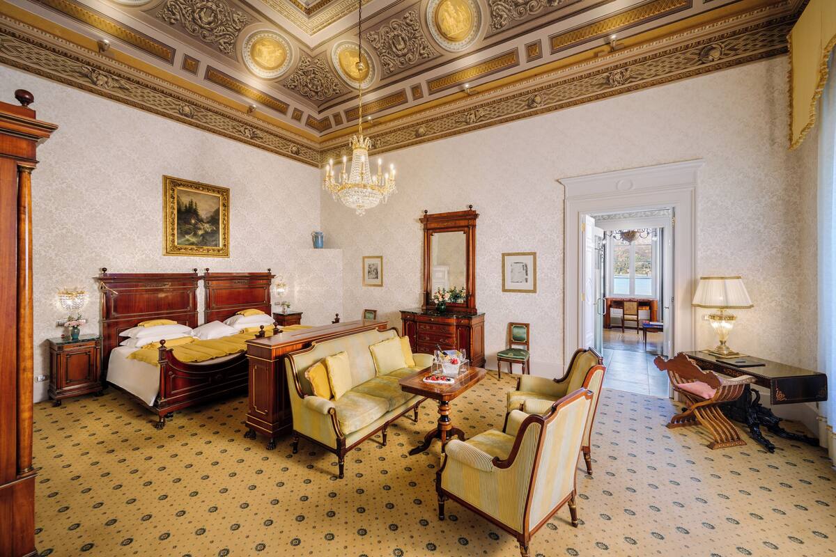 Une pièce spacieuse avec un grand lit, un canapé et une table à manger. Un lustre est suspendu au plafond et un grand miroir orne le mur.