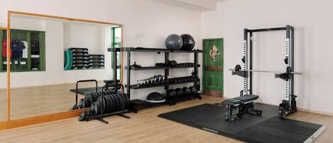 Un gimnasio con equipo de levantamiento de pesas, un espejo y una puerta verde.
