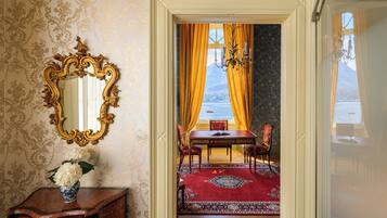 A room with a mirror, a table with chairs, a vase with flowers, and a view of a body of water through a window.