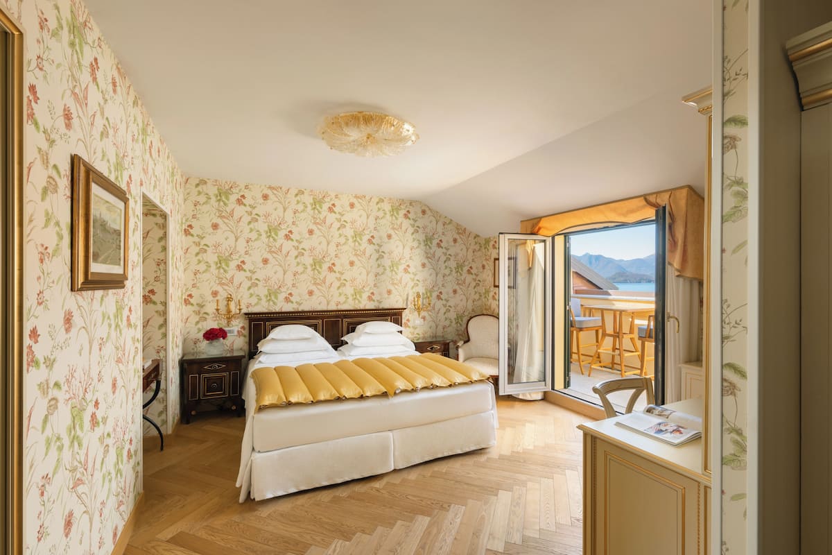 Une chambre à coucher avec un lit, une table de chevet, une chaise, un bureau et une vue sur l’extérieur, grâce à une porte ouverte.