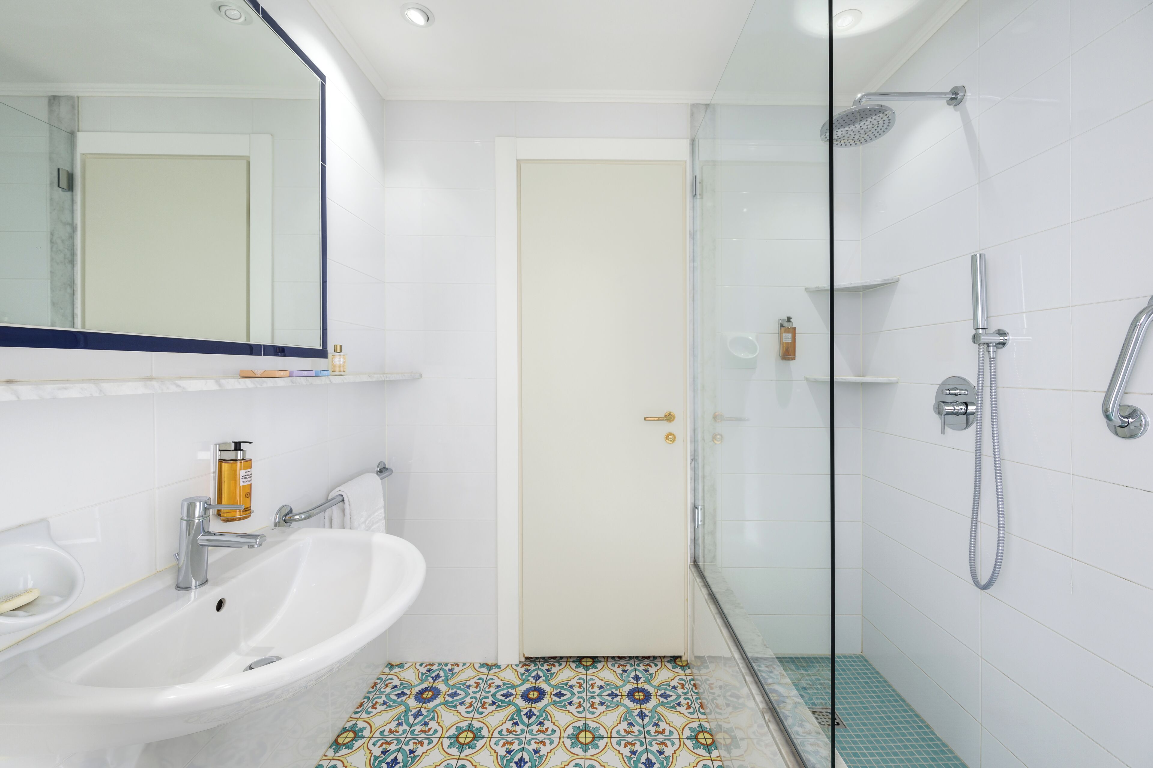 Une salle de bain avec un lavabo blanc, un miroir, une douche et une porte.